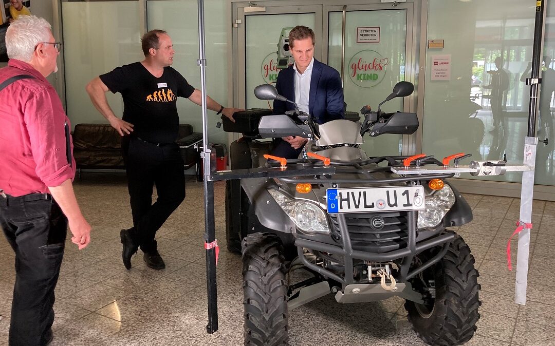 Ein Mann sitzt auf einem Quad, links neben ihm stehen zwei Männer